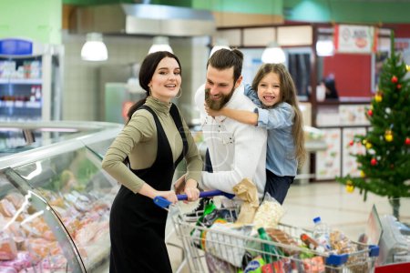 Foto de Familia joven con una niña comprando en un gran supermercado. Concepto de un nuevo año - Imagen libre de derechos