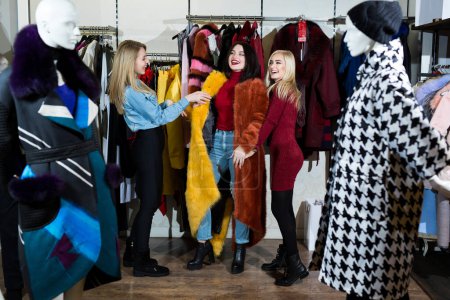Téléchargez les photos : Trois femmes essayant un manteau de fourrure dans le magasin - en image libre de droit