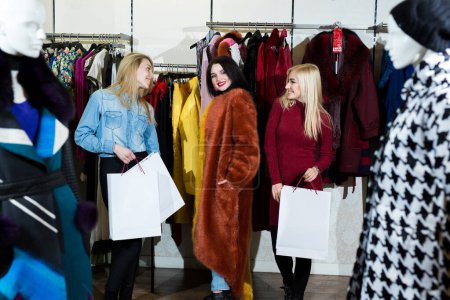 Téléchargez les photos : Trois femmes essayant un manteau de fourrure dans le magasin - en image libre de droit