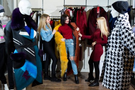 Téléchargez les photos : Trois femmes essayant un manteau de fourrure dans le magasin. - en image libre de droit