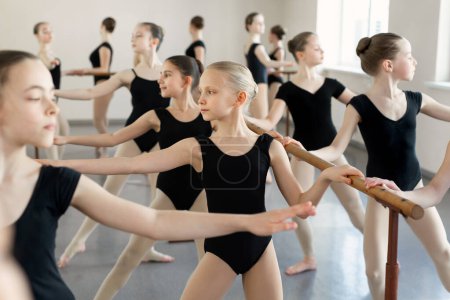 Foto de Bailarinas jóvenes ensayando en la clase de ballet. Realizan diferentes ejercicios coreográficos. Están en diferentes posiciones cerca de la barra de ballet
. - Imagen libre de derechos