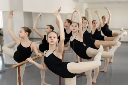 Young ballerinas training at ballet barre. Group of ballet dancers posing near barre in ballet studio. Difference between gymnastics and ballet.
