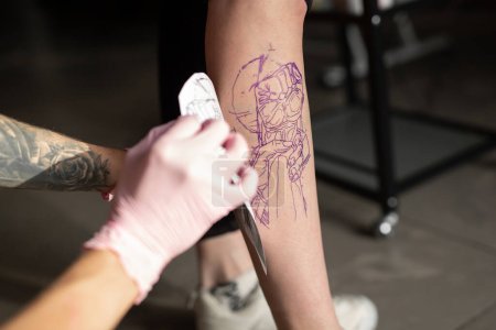 Foto de Recortado tiro de tatuaje artista transferir boceto de tatuaje en el hombro en salón de tatuaje - Imagen libre de derechos