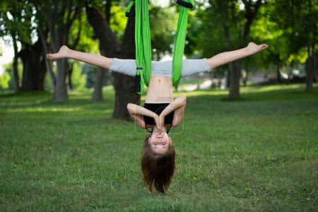 Téléchargez les photos : Petite fille faisant des exercices de yoga avec un hamac dans le parc - en image libre de droit