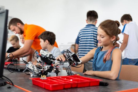 Education, children, technology, science and people concept - group of happy kids with laptop computer building robots at robotics school lesson