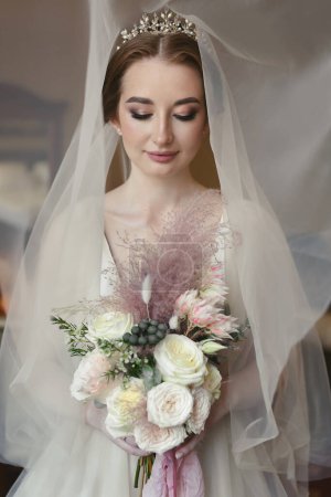 Photo for Portrait of a beautiful young bride on her wedding day with a veil and a bouquet of flowers in her hands. - Royalty Free Image