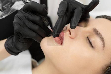 Foto de Primer plano del procedimiento de maquillaje permanente. Maquillaje labial en el salón de cosmetólogos. - Imagen libre de derechos