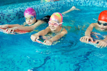 Foto de Grupo de niños y niñas entrenan y aprenden a nadar en la piscina con un instructor. Desarrollo de deportes infantiles. - Imagen libre de derechos