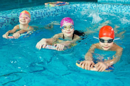 Foto de Grupo de niños y niñas entrenan y aprenden a nadar en la piscina con un instructor. Desarrollo de deportes infantiles. - Imagen libre de derechos