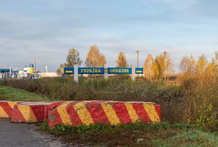 Schild mit der Aufschrift Ukraine am Grenzübergang und einem Betonblock mit roten und gelben Streifen. TEXT TRANSLATION: UKRAINE