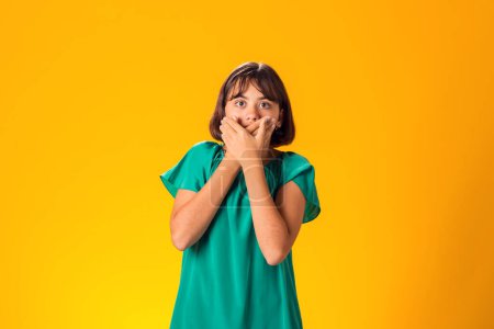 Photo for Scared girl covered mouth with hands over yellow background - Royalty Free Image