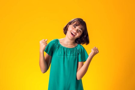 Foto de Niña sonriente mostrando éxito sobre fondo amarillo. Concepto de suerte - Imagen libre de derechos