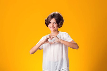 Foto de Niña sonriente mostrando gesto cardíaco sobre fondo amarillo. Concepto de amor - Imagen libre de derechos