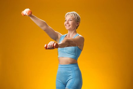 Photo for Fitness woman with short blond hair holding dumbbells isolated on yellow background. Activity and healthcare concept - Royalty Free Image