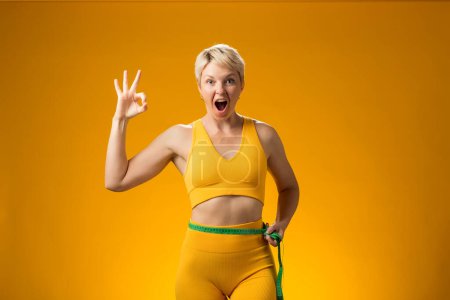 Téléchargez les photos : Femme fitness aux cheveux courts avec ruban à mesurer isolé sur fond jaune. Perte de poids et concept de santé - en image libre de droit