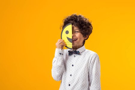 Téléchargez les photos : Garçon heureux tenant des visages heureux et tristes sur deux morceaux de papier mémo. émoticône. - en image libre de droit
