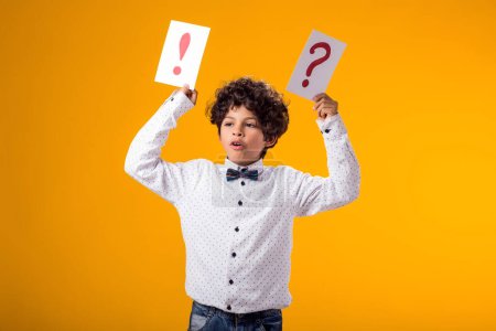 Foto de Retrato de niño sosteniendo signo de interrogación y tarjetas de signo de exclamación sobre fondo amarillo. Lluvia de ideas y concepto de elección - Imagen libre de derechos