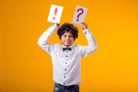 Photo for Portrait of child boy holding question mark and exclamation point cards over yellow background. Brainstorming and choice concept - Royalty Free Image
