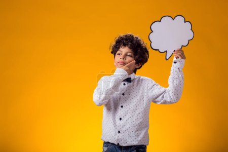 Téléchargez les photos : Enfant garçon réfléchi tenant bulle de discours sur fond jaune. Concept d'éducation et de curiosité - en image libre de droit