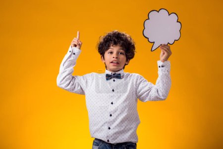 Téléchargez les photos : Enfant garçon réfléchi tenant bulle de discours sur fond jaune. Concept d'éducation et de curiosité - en image libre de droit