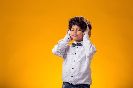 Foto de Retrato de niño con auriculares escuchando música y bailando sobre fondo amarillo. Concepto de ocio y estilo de vida - Imagen libre de derechos