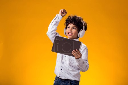 Foto de Retrato de niño niño usando tableta digital y auriculares y jugando videojuego. Concepto de adicción al ocio y al gadget. - Imagen libre de derechos