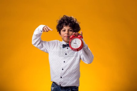 Photo for Portrait of child boy holding alarm clock over yellow background. Time management concept - Royalty Free Image