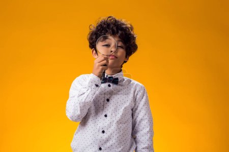 Photo for Portrait of child boy looking through magnifier over yellow background. Education and curiosity concept - Royalty Free Image