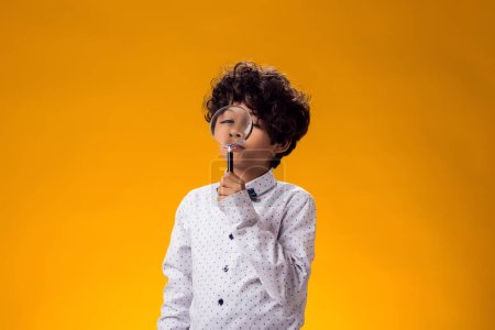 Téléchargez les photos : Portrait d'enfant garçon regardant à travers loupe sur fond jaune. Concept d'éducation et de curiosité - en image libre de droit