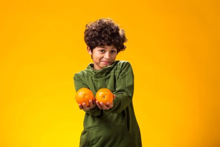 Photo for Portrait of child boy holding orange fruits over yellow background. Healthy food concept - Royalty Free Image