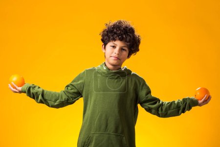 Téléchargez les photos : Portrait d'un enfant garçon tenant des fruits orange sur fond jaune. Concept d'alimentation saine - en image libre de droit