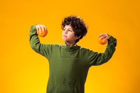 Foto de Retrato de niño sosteniendo frutas naranjas sobre fondo amarillo. Concepto de comida saludable - Imagen libre de derechos
