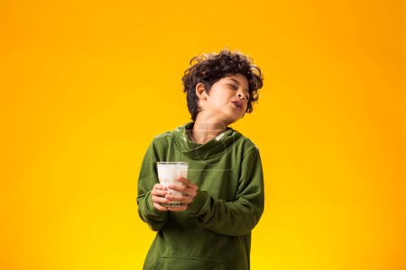 Photo for Lactose intolerance. Dairy intolerant unhappy child boy holding glass of milk over yellow background. - Royalty Free Image