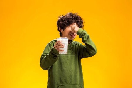 Foto de Intolerancia a la lactosa. Lácteos intolerante infeliz niño sosteniendo vaso de leche sobre fondo amarillo. - Imagen libre de derechos