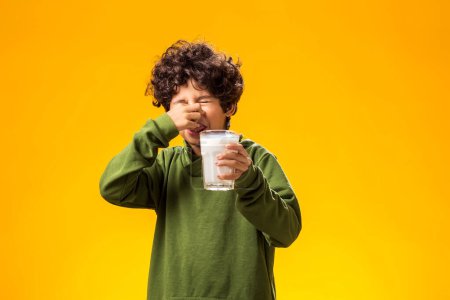 Téléchargez les photos : Intolérance au lactose. Intolérance laitière enfant malheureux garçon tenant verre de lait sur fond jaune. - en image libre de droit