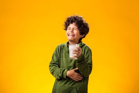 Photo for Lactose intolerance. Dairy intolerant unhappy child boy holding glass of milk and feeling abdominal pain over yellow background. - Royalty Free Image