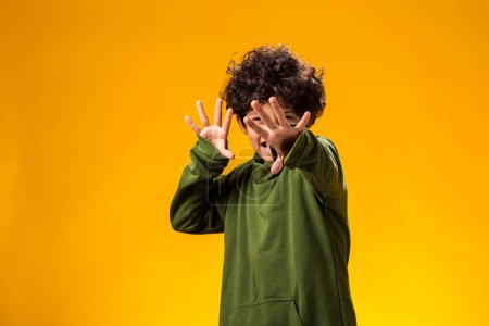 Photo for Ortrait of afraid child boy showing stop gesture on yellow background. Bulling and negative emotions concept - Royalty Free Image