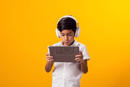Foto de Retrato de niño con auriculares y tableta jugando videojuego. Concepto de adicción al ocio y al gadget - Imagen libre de derechos