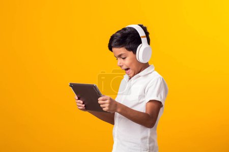 Téléchargez les photos : Portrait de garçon enfant avec casque et tablette jouant au jeu vidéo. Loisirs et gadget addiction concept - en image libre de droit