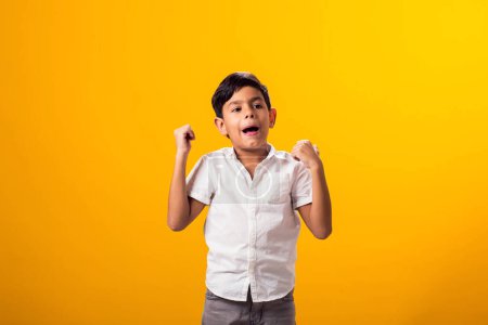 Téléchargez les photos : Portrait d'un petit garçon montrant un geste gagnant sur fond jaune. Concept de réussite et de victoire - en image libre de droit