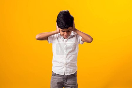 Photo for Portrait of kid boy covering ears over yellow background. Noise, stress and childhood concept - Royalty Free Image