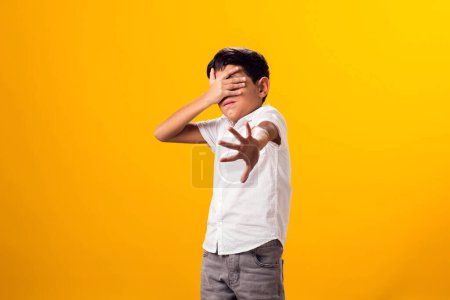 Téléchargez les photos : Portrait d'un garçon effrayé montrant un geste d'arrêt et couvrant les yeux sur un fond jaune. - en image libre de droit