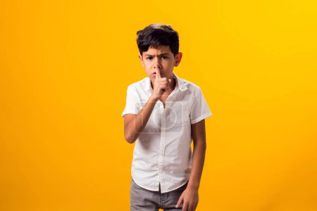 Téléchargez les photos : Portrait de garçon enfant tenant le doigt sur les lèvres et montrant un geste de silence sur fond jaune. - en image libre de droit