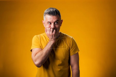 Téléchargez les photos : Portrait de l'homme stressé et nerveux avec les mains sur la bouche mordant ongles sur fond jaune. Problème d'anxiété. - en image libre de droit