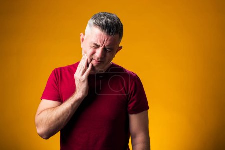 Téléchargez les photos : Portrait d'un homme souffrant de maux de dents, sur fond jaune. La main sur la joue. Le concept des personnes, des soins et de la médecine - en image libre de droit