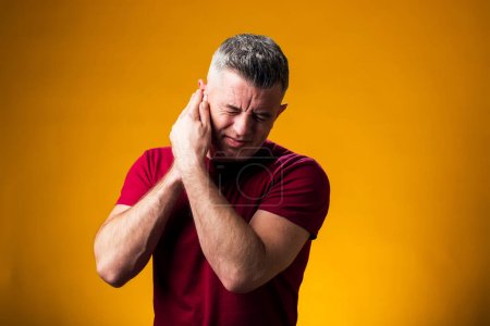 Téléchargez les photos : Portrait d'un homme souffrant de douleurs à l'oreille. Main sur l'oreille, sur fond jaune. Le concept des personnes, des soins et de la médecine - en image libre de droit