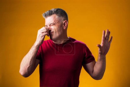 Foto de Retrato del hombre que muestra disgusto y se cubre la nariz con la mano sobre un fondo amarillo aislado, el tipo rechaza el mal olor y rechaza el hedor - Imagen libre de derechos