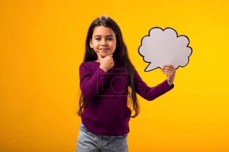 Foto de Retrato de niña reflexiva sosteniendo la tarjeta de burbuja nube sobre fondo amarillo. Concepto de ensueño - Imagen libre de derechos