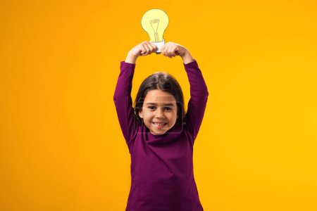 Téléchargez les photos : Portrait d'une enfant réfléchie tenant une ampoule en papier au-dessus de la tête. Succès, motivation, vainqueur, génie, concept d'idée - en image libre de droit