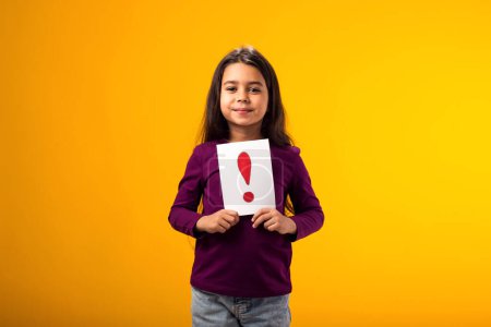 Foto de Un retrato de una niña sonriente sosteniendo una tarjeta de signo de exclamación. Concepto de niños, ideas y conocimientos - Imagen libre de derechos